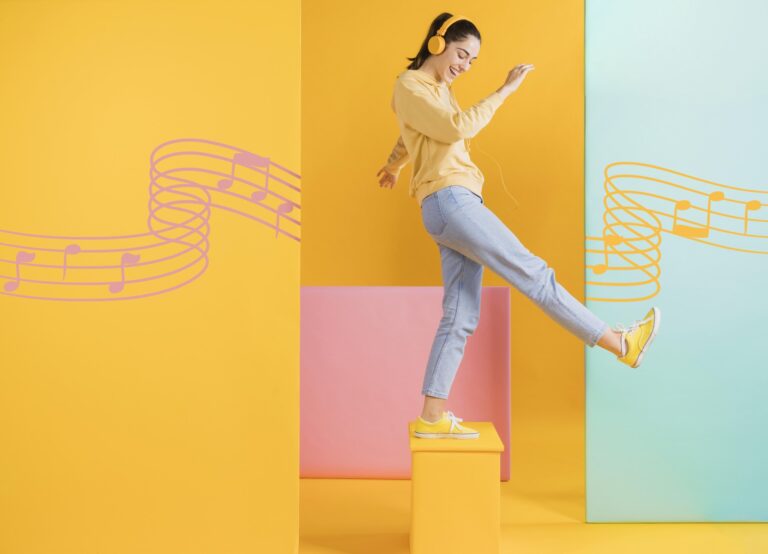 Findo com diferentes tons de amarelo, rosa e azul. À frente, uma mulher com fones de ouvido vestindo uma blusa amarela, calça azul, e tênis amarelo, se apoia em um pé só em cima de um suporte quadrado na cor amarela.