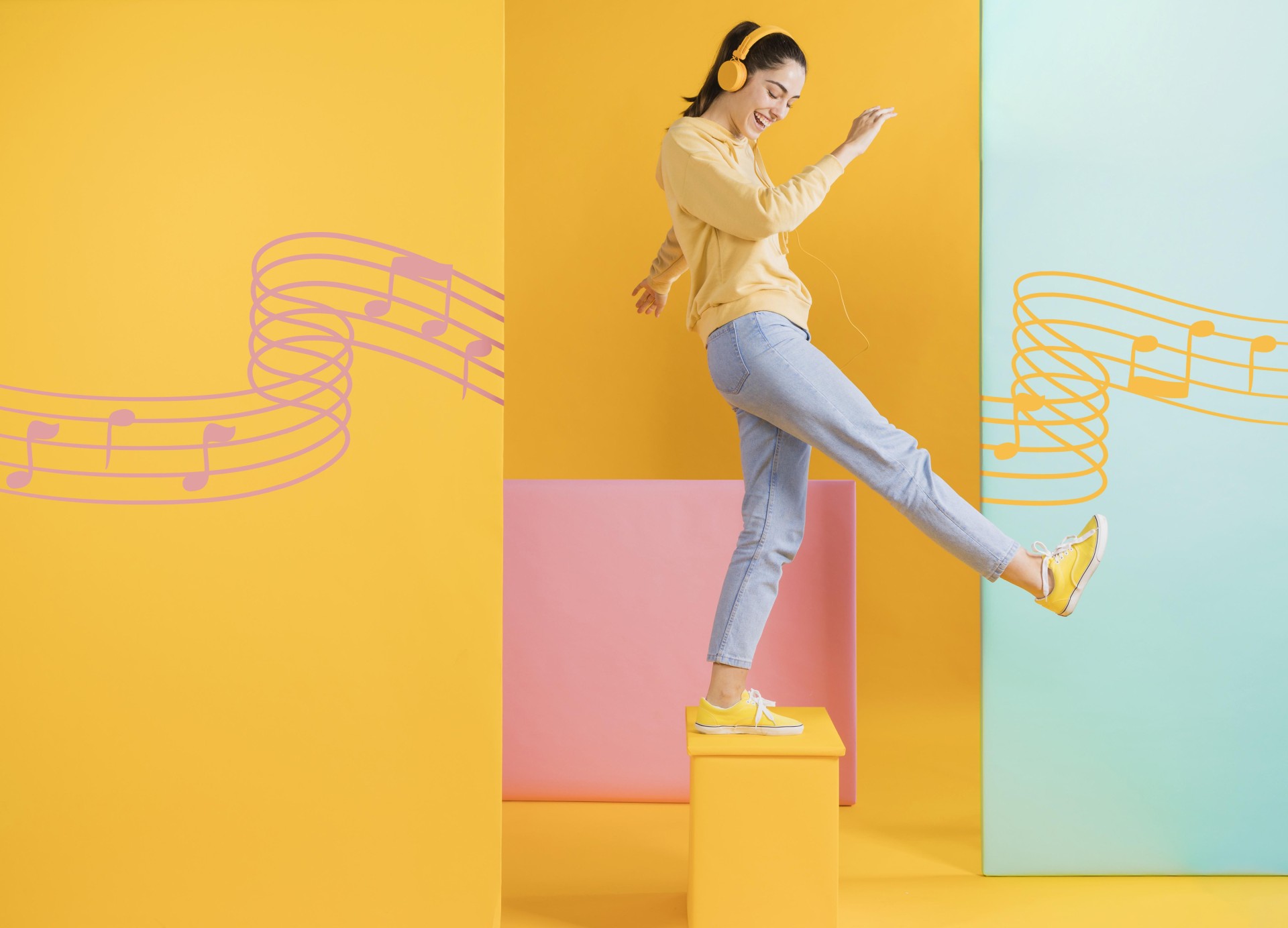 Findo com diferentes tons de amarelo, rosa e azul. À frente, uma mulher com fones de ouvido vestindo uma blusa amarela, calça azul, e tênis amarelo, se apoia em um pé só em cima de um suporte quadrado na cor amarela.