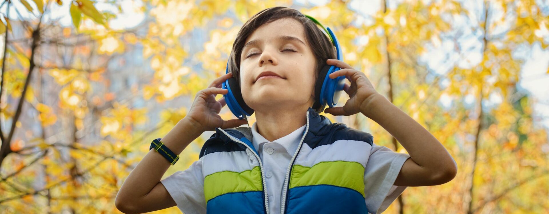 Um menino ouve música em fones de ouvido em meio à colorida folhagem de outono.