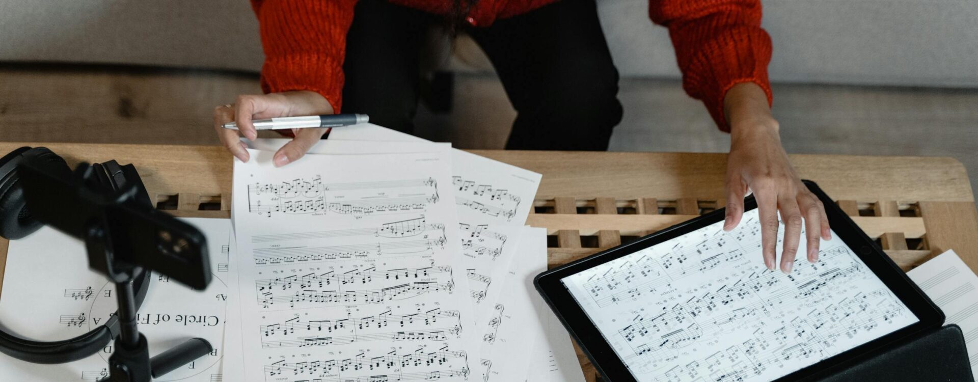 Um músico analisa partituras em um tablet cercado por papelada.