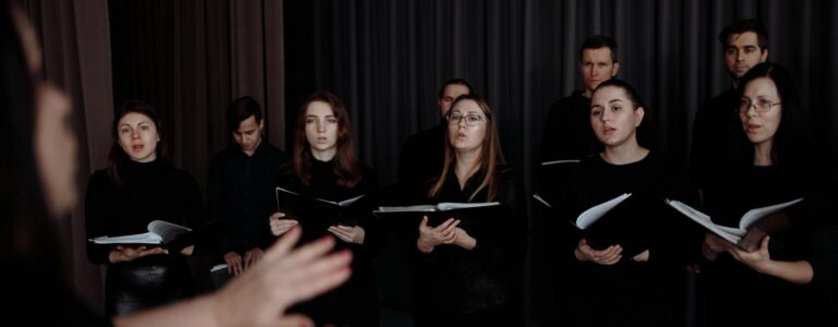 Um grupo de coreal cantando, conduzidos por um maestro.